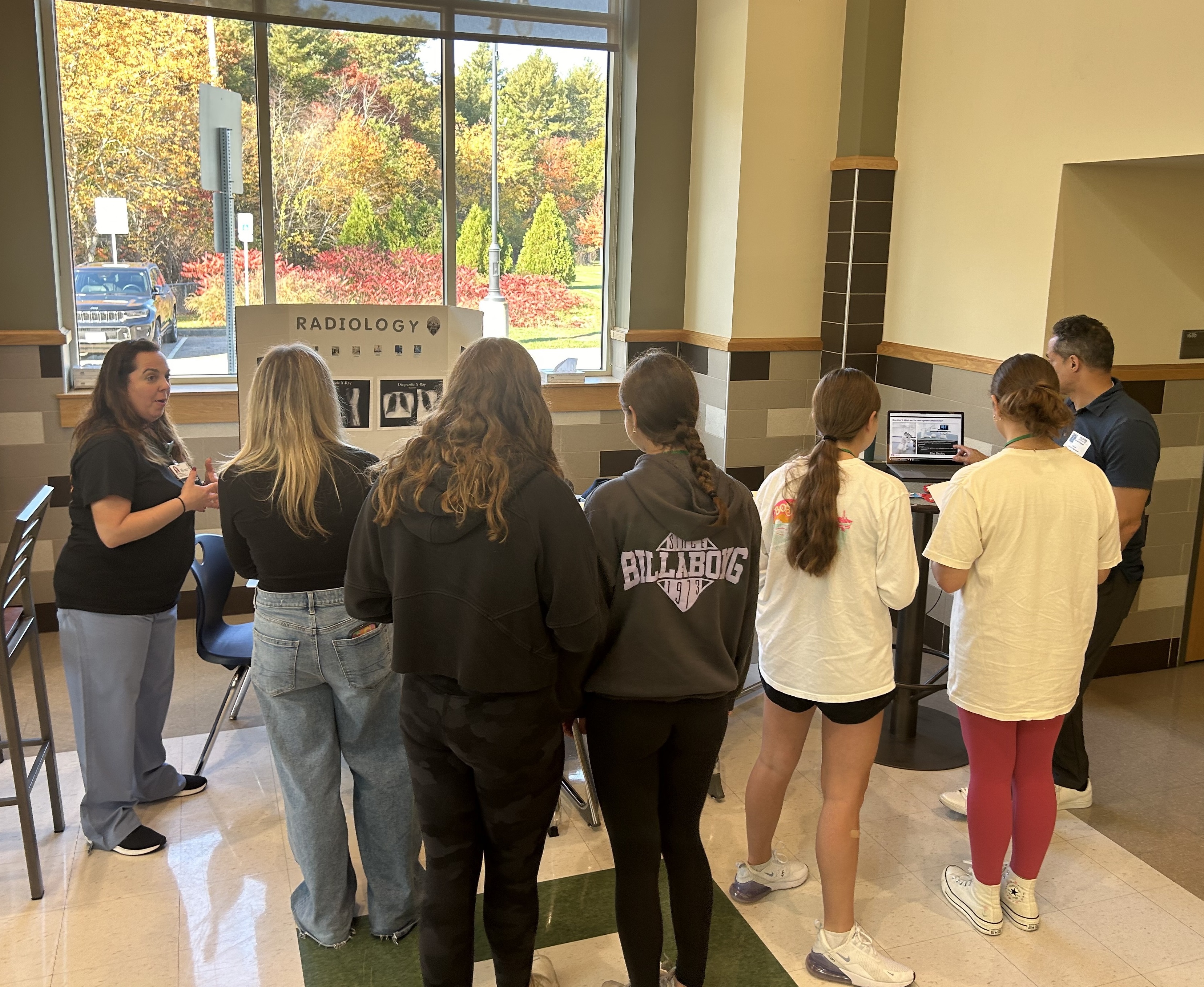 Students stand in front of display boards as two South Shore Health colleagues share info on healthcare careers at a high school career event.