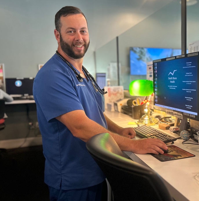 South Shore Health Urgent Care provider Benjamin Hixon, PA-C in front of computer monitor