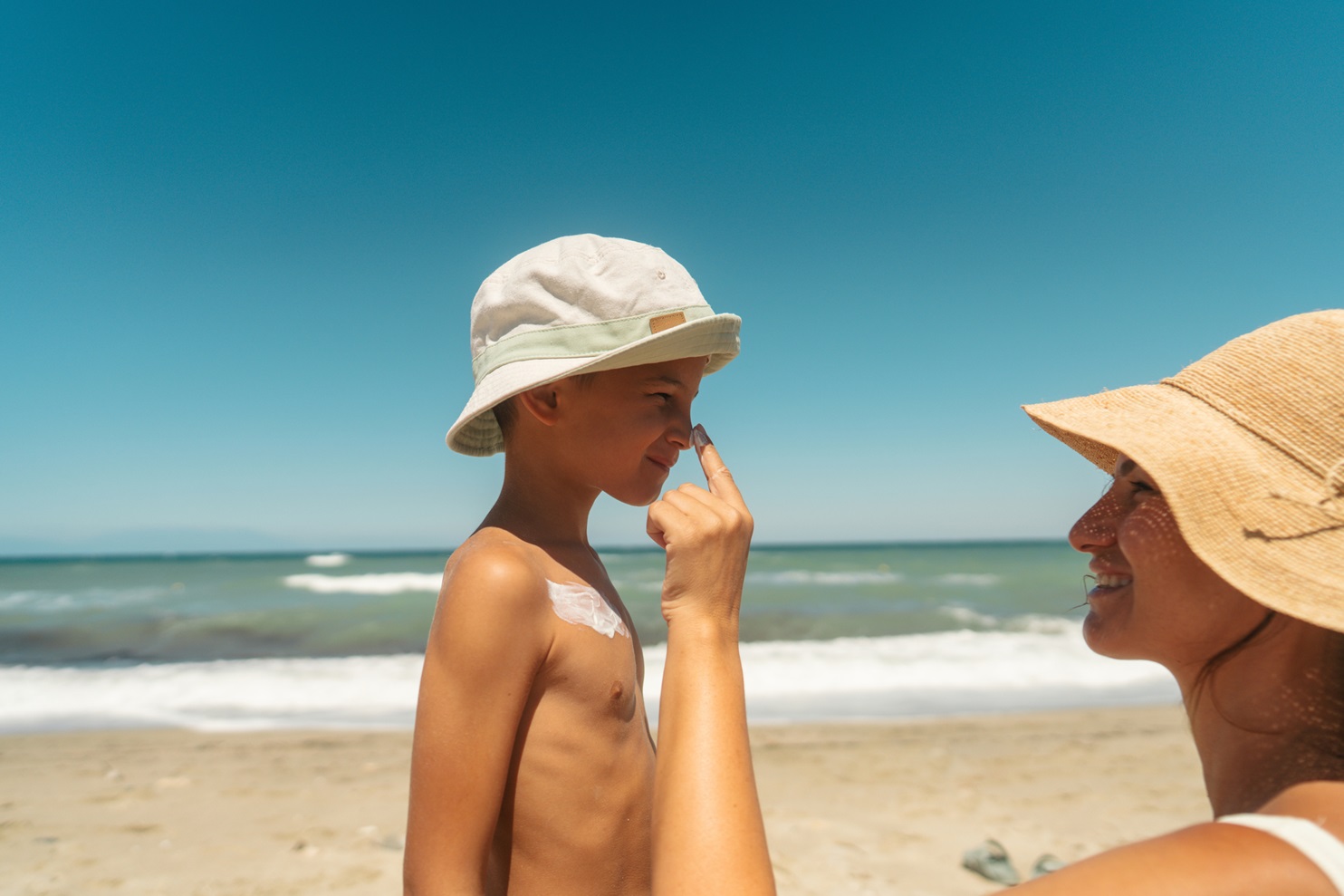 A woman puts sunscreen on a boy's nose at the beach