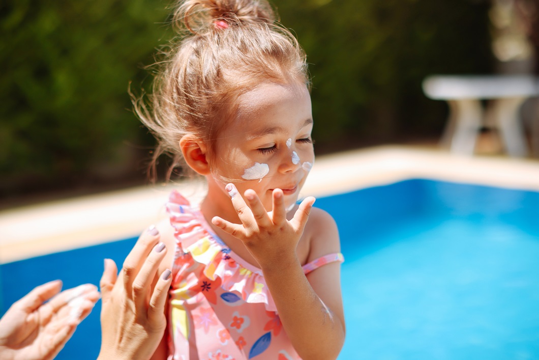 Putting sunscreen on a little girl by the pool