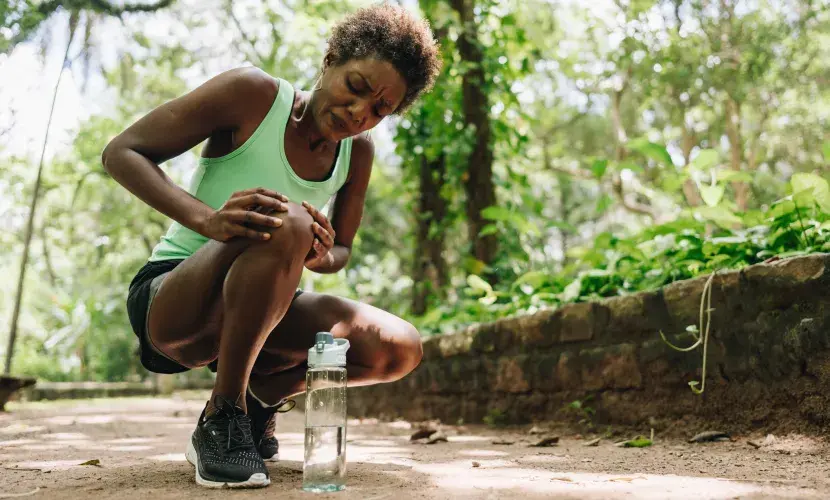 A black woman out for a run bends down to rub her arthritic knee
