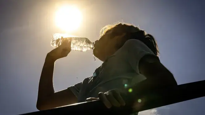 A woman drinking a bottle of water in the hot sun