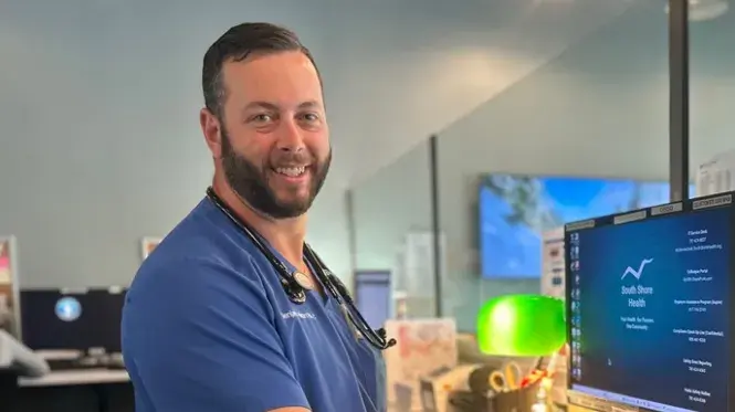 South Shore Health Urgent Care provider Benjamin Hixon, PA-C in front of computer monitor