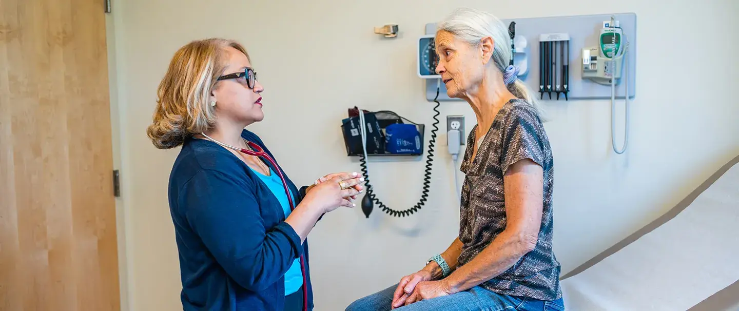 Leyda Delgado, MD of South Shore Medical Center talks to a female patient as she sits on an exam table.