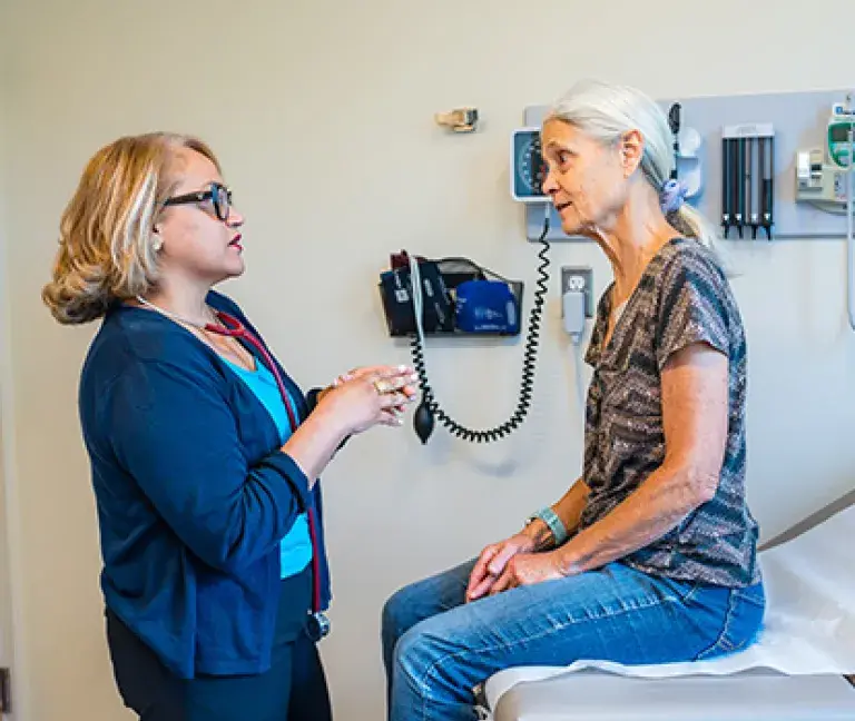 Leyda Delgado, MD of South Shore Medical Center talks to a female patient as she sits on an exam table.