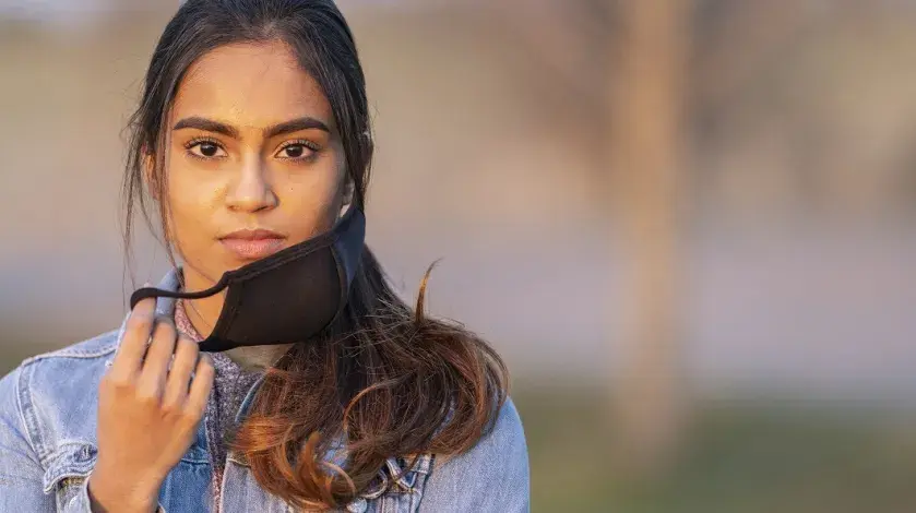 A young woman taking off her face mask