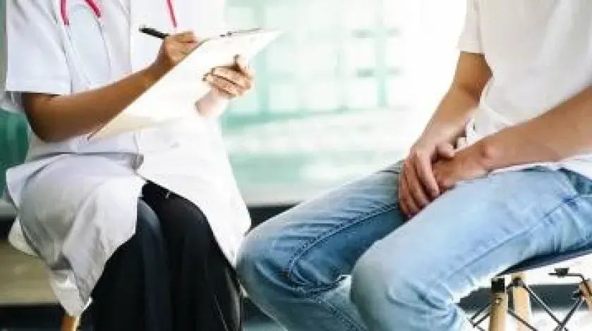 A female provider writes in a chart while talking with a young male patient