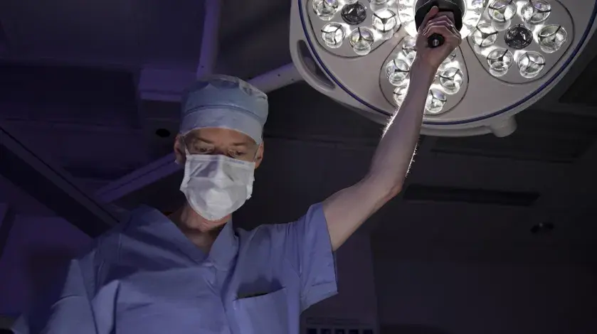 James Stephen, MD, wearing surgical clothing, adjusts an overhead light above an operating table