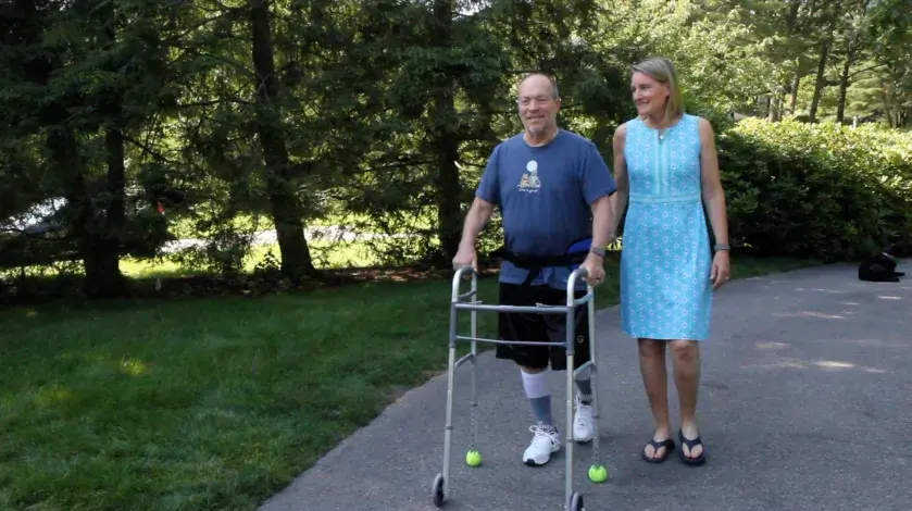 Ed, using a walker, walks next to his wife, Sara, in the driveway of their Duxbury home.