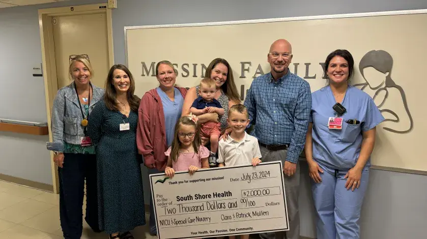 Patrick, Clara, and the Mullen Family pose for a photo with their $2,000 donation check and members of the South Shore Health NICU/Special Care Nursery Team.