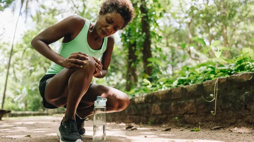 A black woman out for a run bends down to rub her arthritic knee