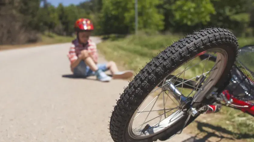 a young boy sits on the sidewalk in the background holding his knee, with his bike in the foreground