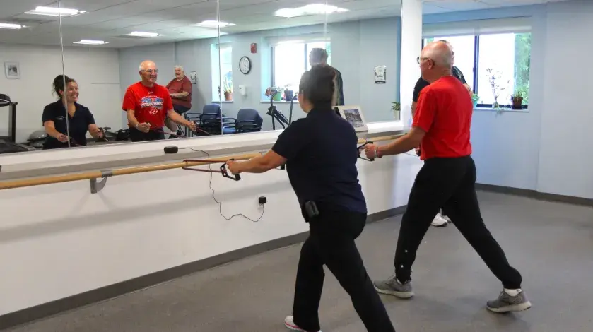 Jen and a participant in her class stand in front of a mirror stretching with resistance bands