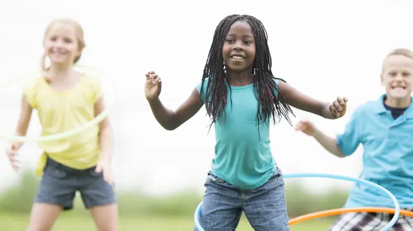 Three young kids play with hula hoops in a park or playground setting.