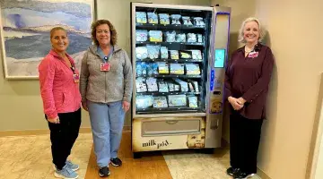 Three colleagues from South Shore Hospital stand next to a MilkPod vending machine.