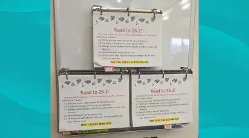 Three binders hanging on a wall containing tracking sheets for South Shore Health's 26.2 Challenge.