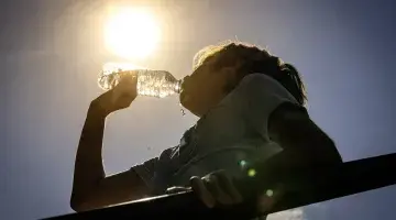 A woman drinking a bottle of water in the hot sun