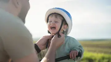 A little boy smiles as his dad adjusts his bike helmet before a bike ride.