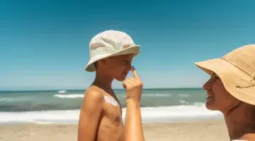 A woman puts sunscreen on a boy's nose at the beach