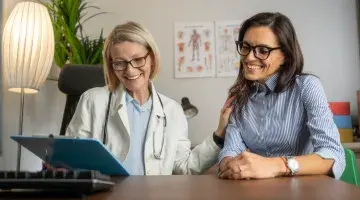 A female provider holding a chart at a desk with a middle aged female patient