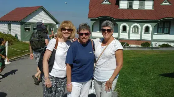 Three women pose for a photo in front of a lighthouse on an outing with The Friends of South Shore Health.
