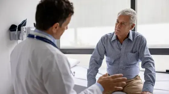 A doctor consults with an older male patient in an exam room.